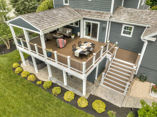 Elevated back deck with roof cover, seating area, and dining setup connected by staircase to backyard.