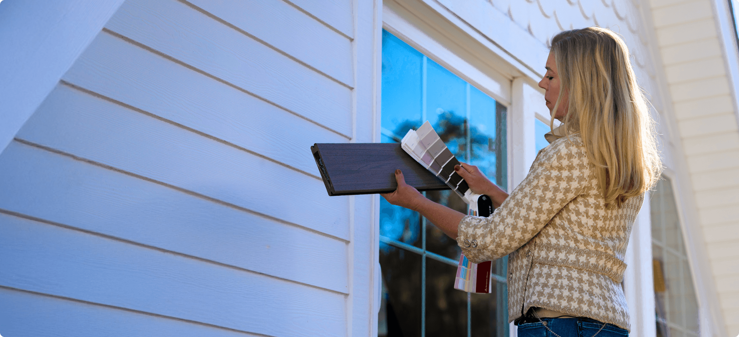 Person Comparing Color Swatches To Composite Deck Board And House