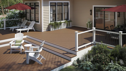 Brown composite deck with white railing, lounge chairs, and patio umbrellas attached to beige house.